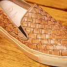 Close view of woven brown slip-on shoes on a wooden surface