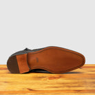 Outsole of Dark brown leather ankle boot with zipper on a wooden surface and light gray background