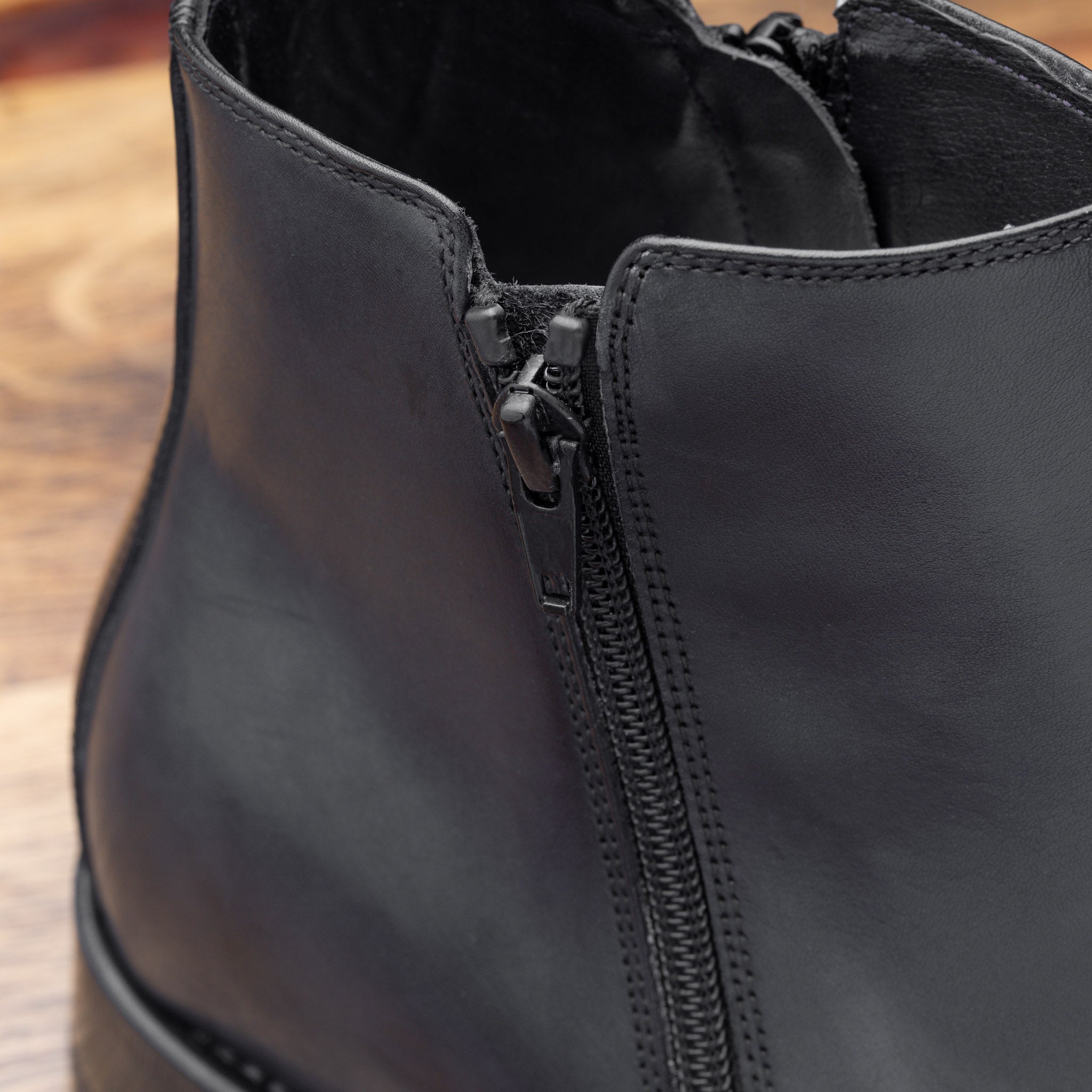 Close-up of Dark brown leather ankle boot with zipper on a wooden surface