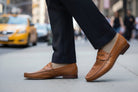 Brown loafers worn on a city street with a blurred background