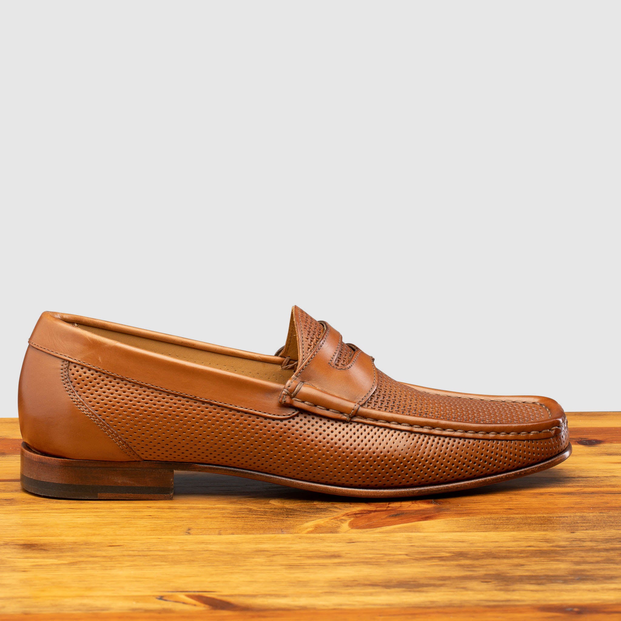 Brown leather loafer on a wooden surface with a light gray background
