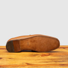 Outsole of Brown leather loafer on a wooden surface with a light gray background