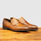 A pair of Chestnut leather loafer on a wooden surface with a light gray background
