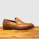 Chestnut leather loafer on a wooden surface with a light gray background