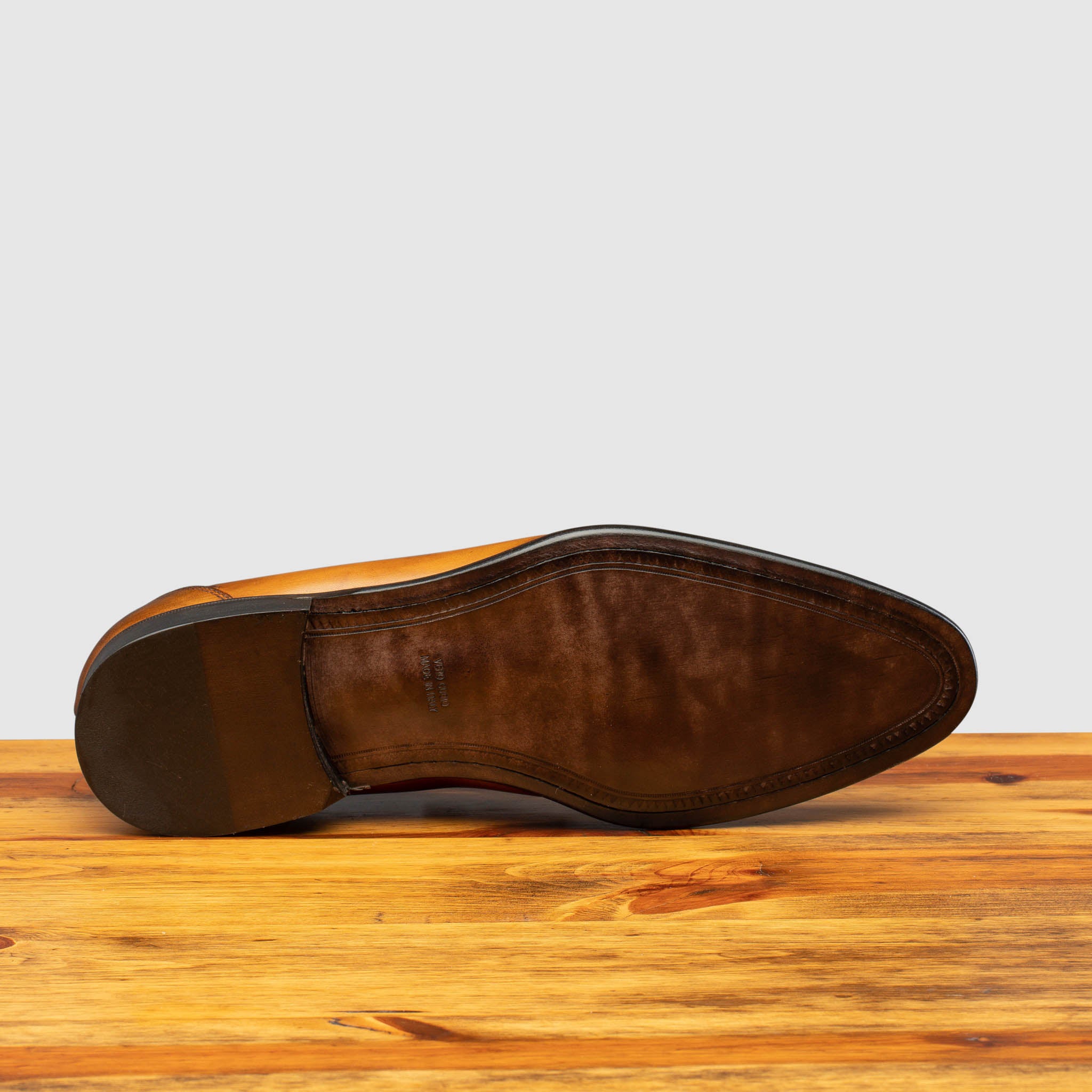 Outsole of Chestnut leather loafer on a wooden surface with a light gray background
