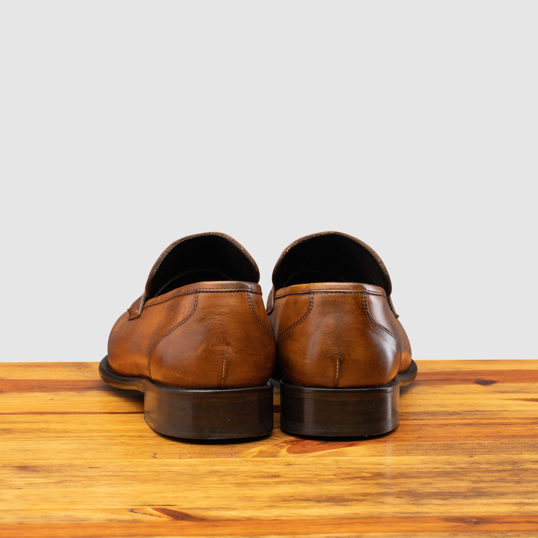 A pair of Chestnut leather loafer on a wooden surface with a light gray background