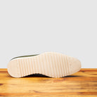 Outsole of Green leather shoe on a wooden surface with a gray background