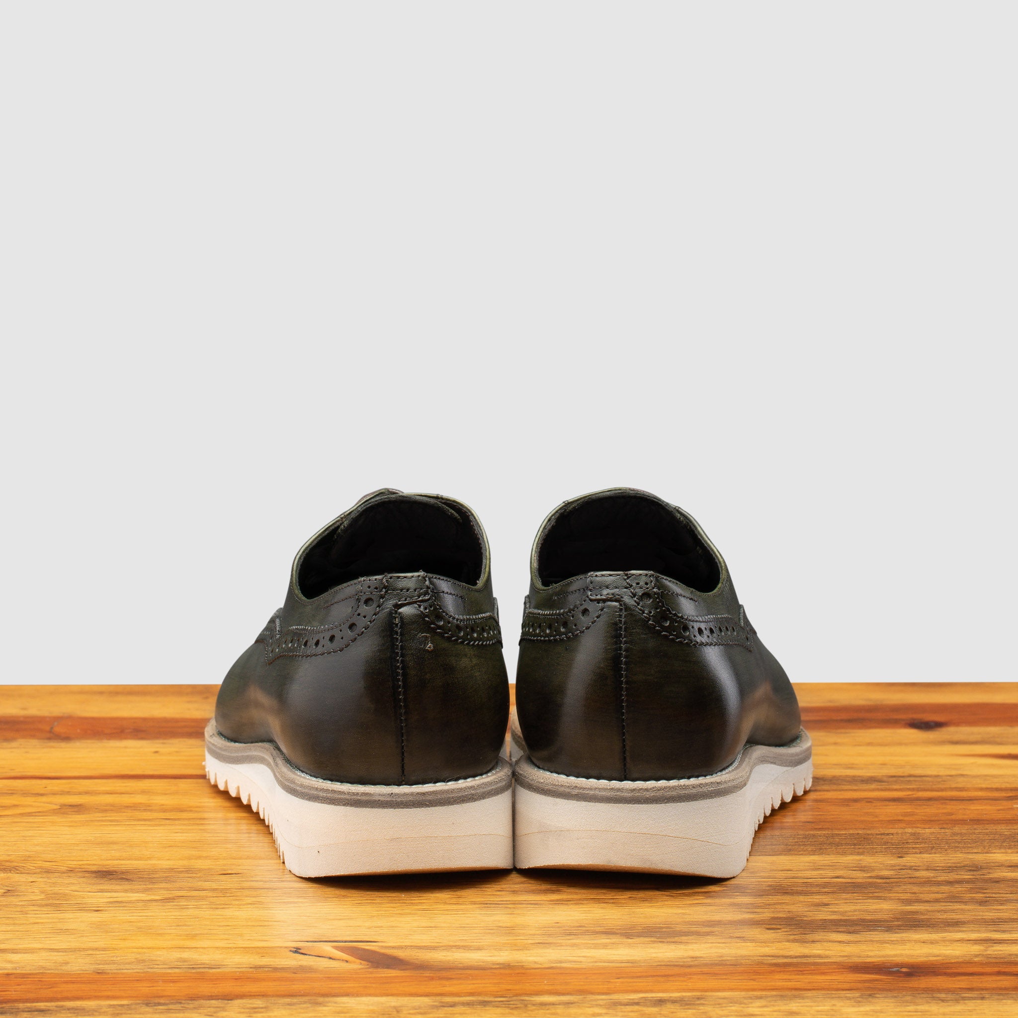 Back view of Green leather shoe on a wooden surface with a gray background