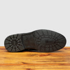 Outsole of Black leather boot on a wooden surface with a light gray background