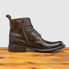 Brown leather boot on a wooden surface with a light gray background