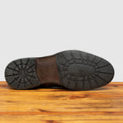 Outsole of Brown leather boot on a wooden surface with a light gray background