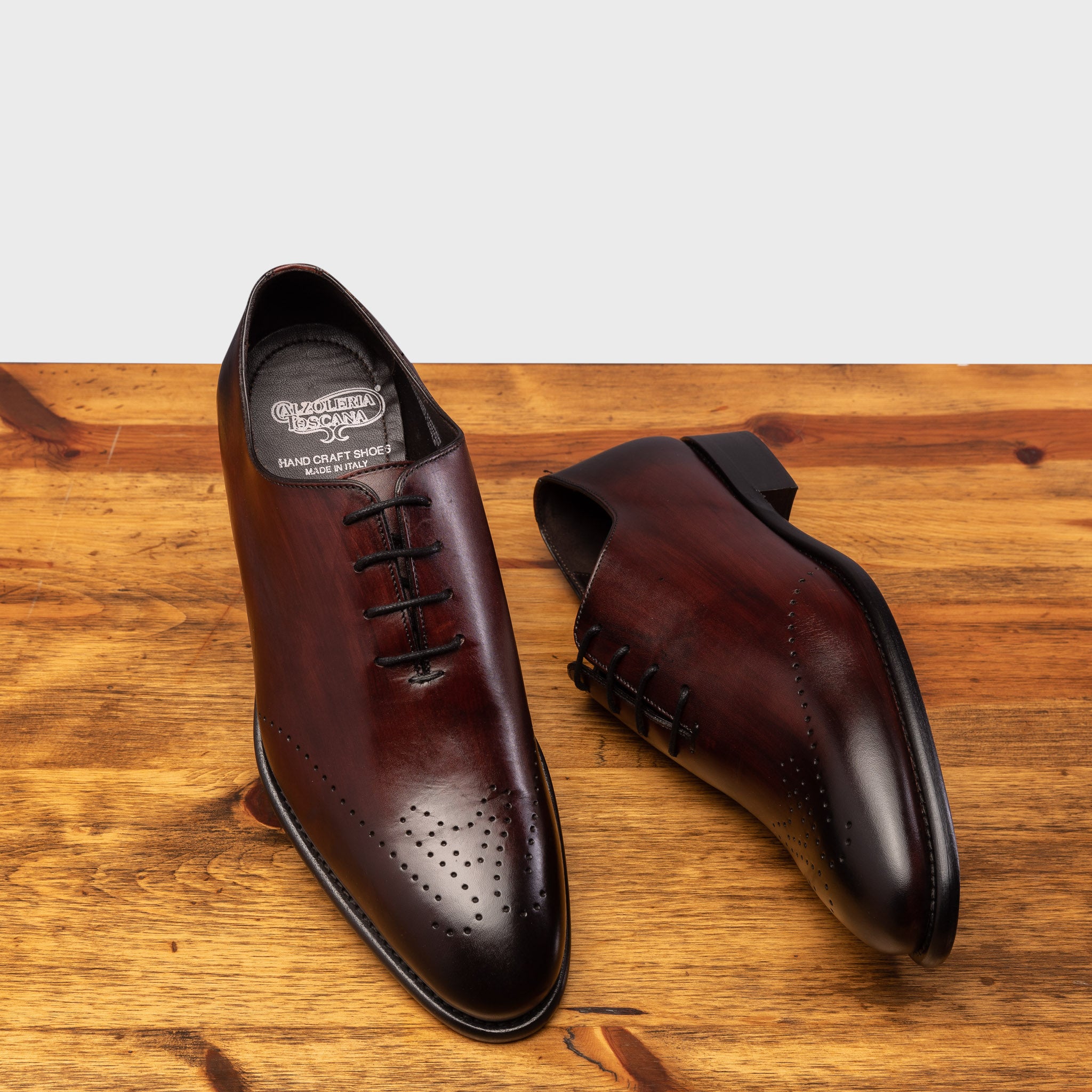 A Pair of Burgundy leather dress shoe on a wooden surface with a light gray background