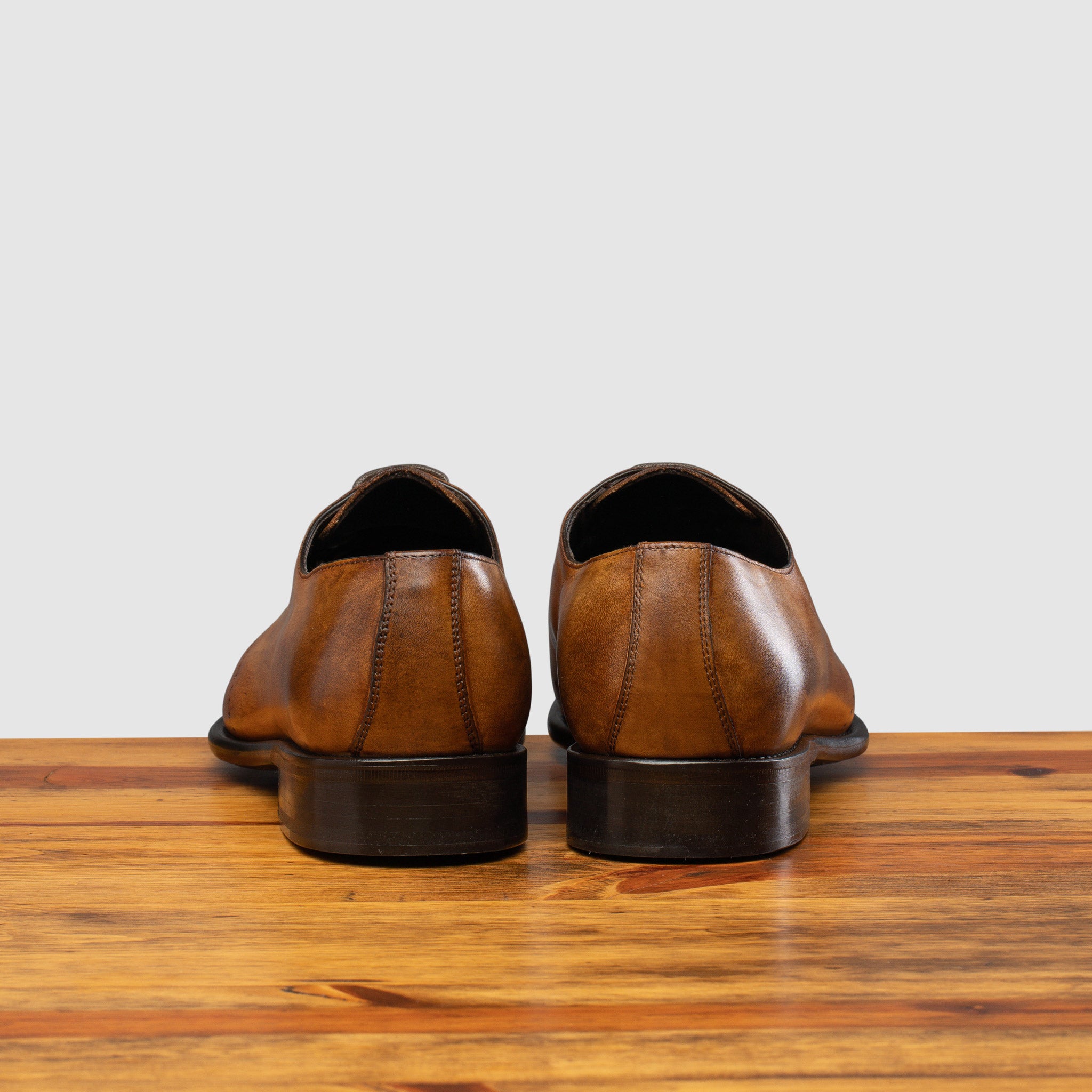 A Pair of chestnut wholecut leather Oxford shoe, displayed on a wooden surface.
