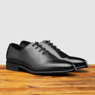 A Pair of Graphite leather dress shoe on a wooden surface with a light gray background