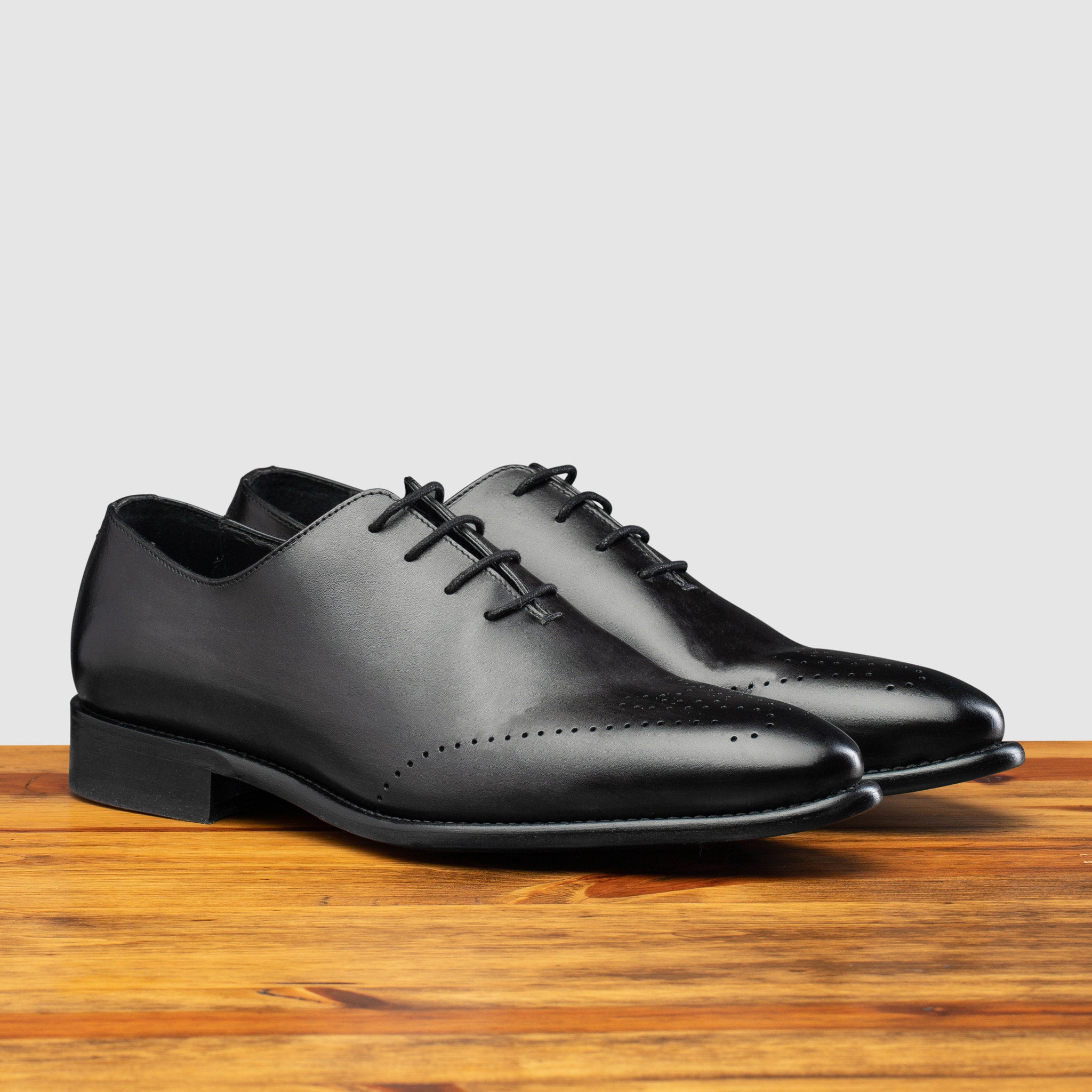 A Pair of Graphite leather dress shoe on a wooden surface with a light gray background