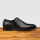 Graphite leather dress shoe on a wooden surface with a light gray background