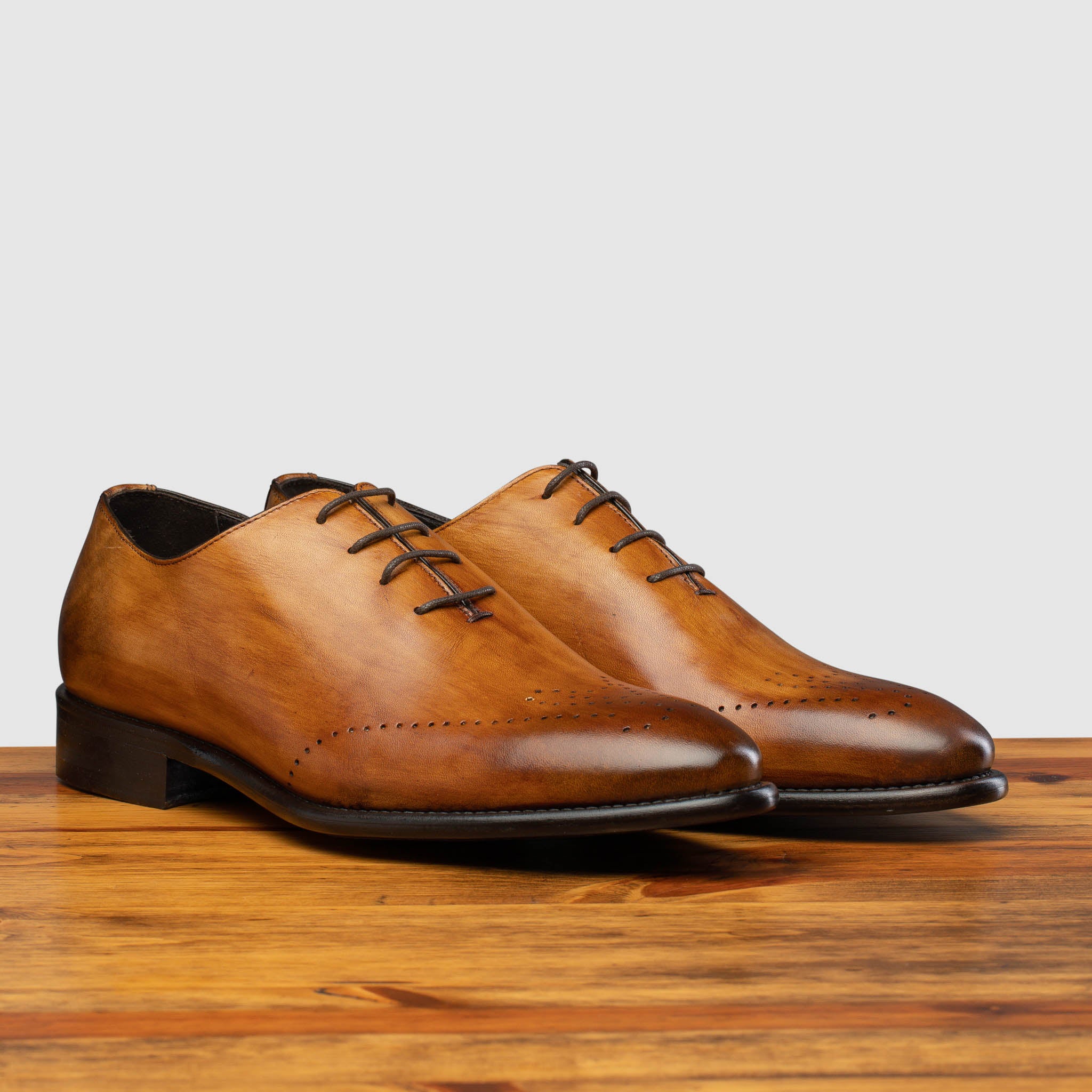 A Pair of chestnut wholecut leather Oxford shoe, displayed on a wooden surface.