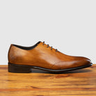 A chestnut wholecut leather Oxford shoe, displayed on a wooden surface.