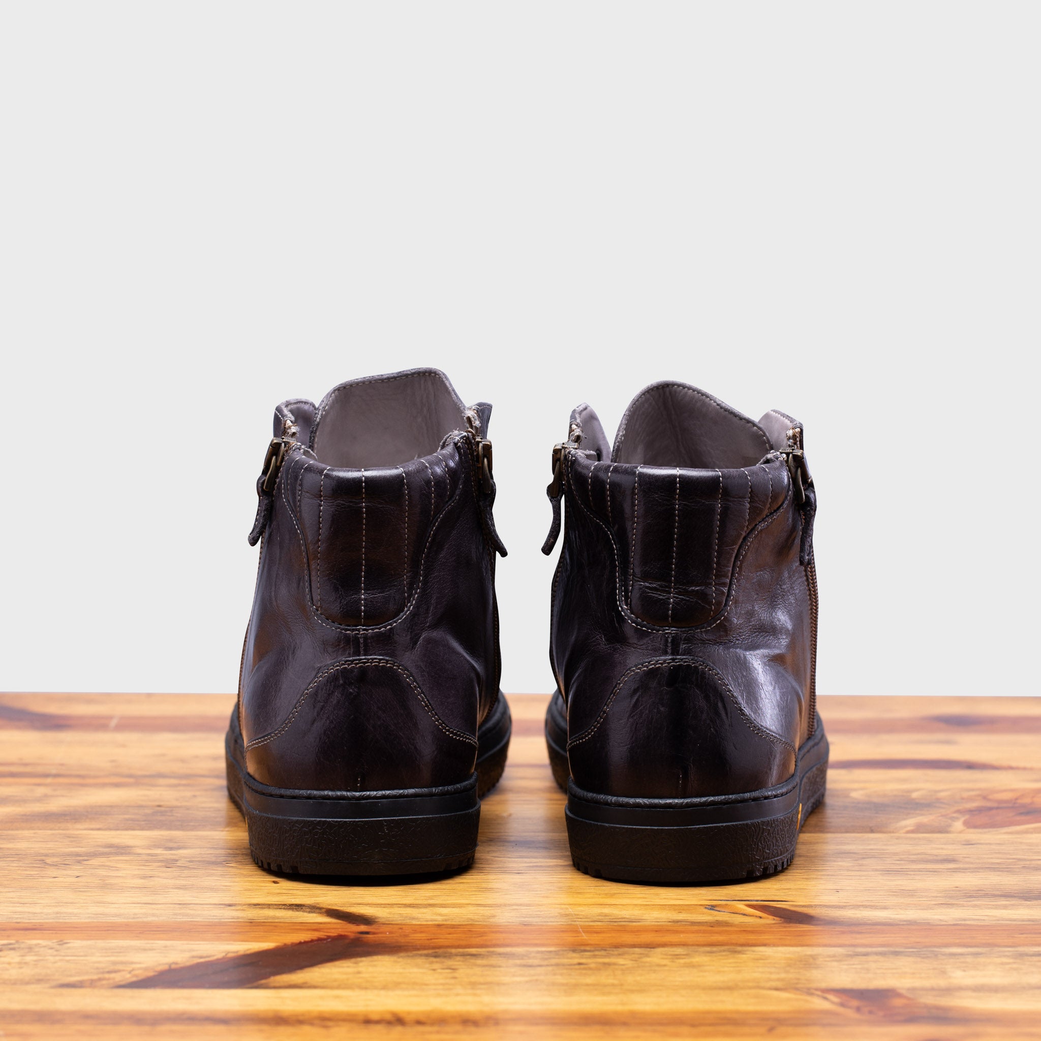 Back view of Brown leather high-top sneaker with a visible Vibram logo on a wooden surface.
