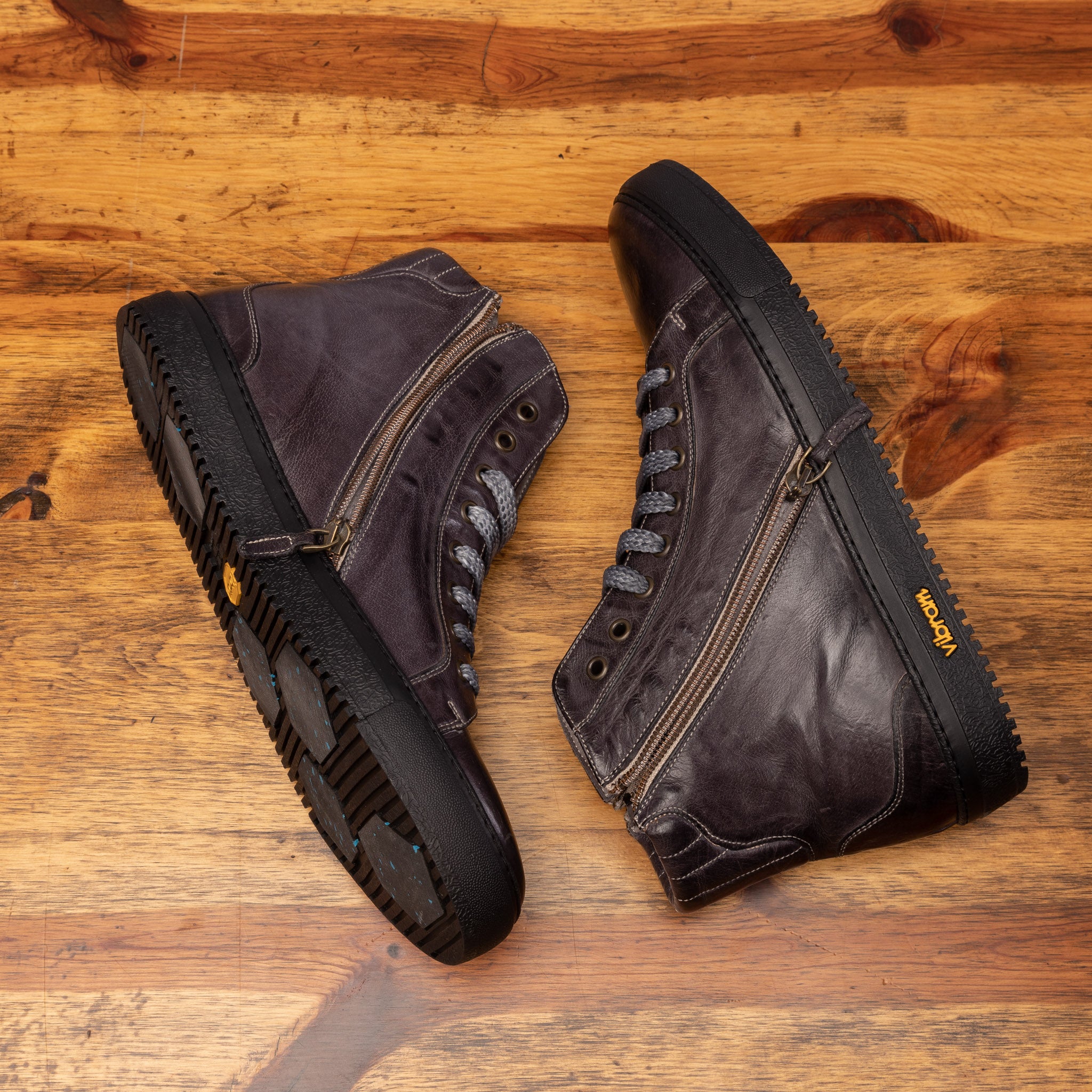 Pair of Brown leather high-top sneaker with a visible Vibram logo on a wooden surface.