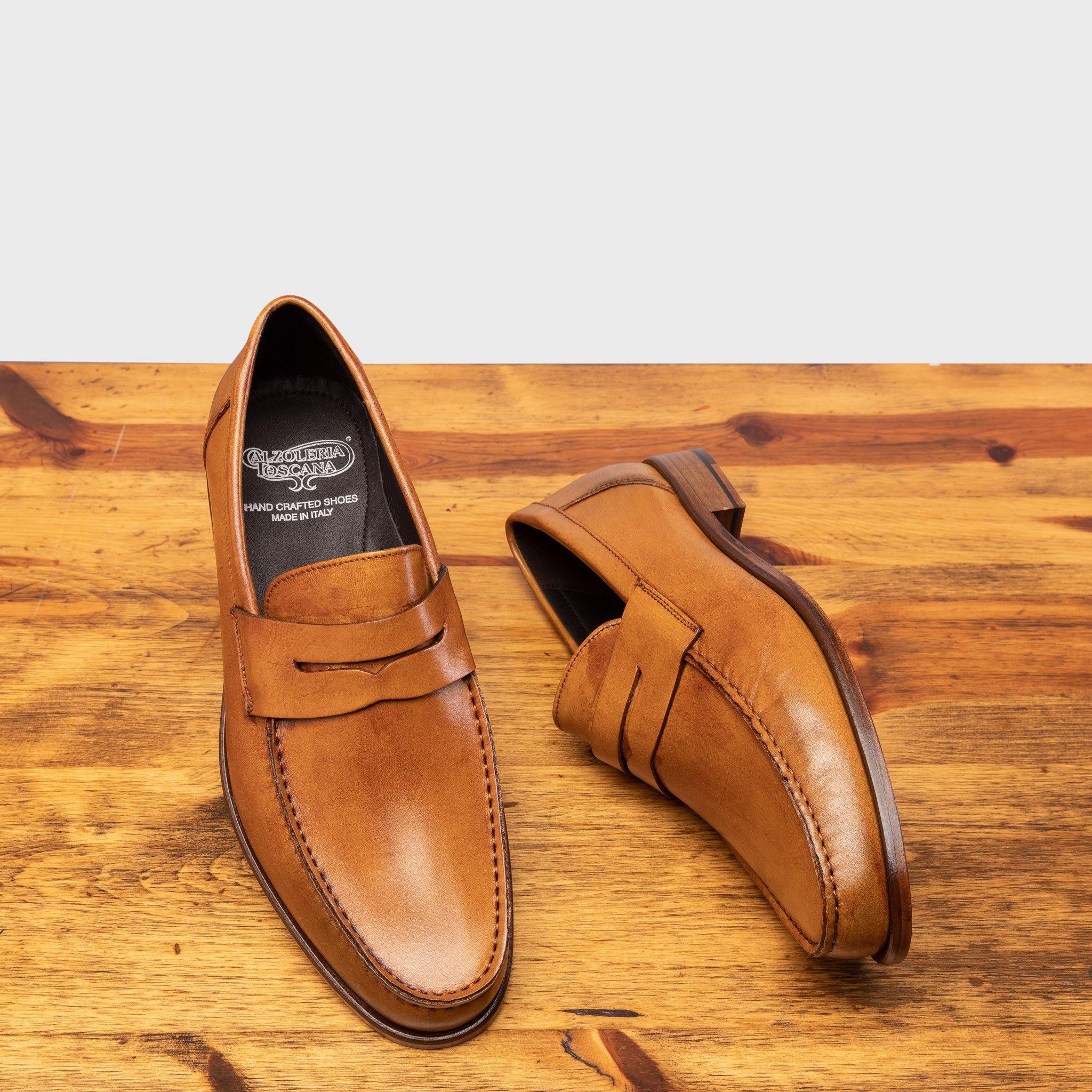 Pair of Dark Caramel leather loafer on a wooden surface with a light gray background