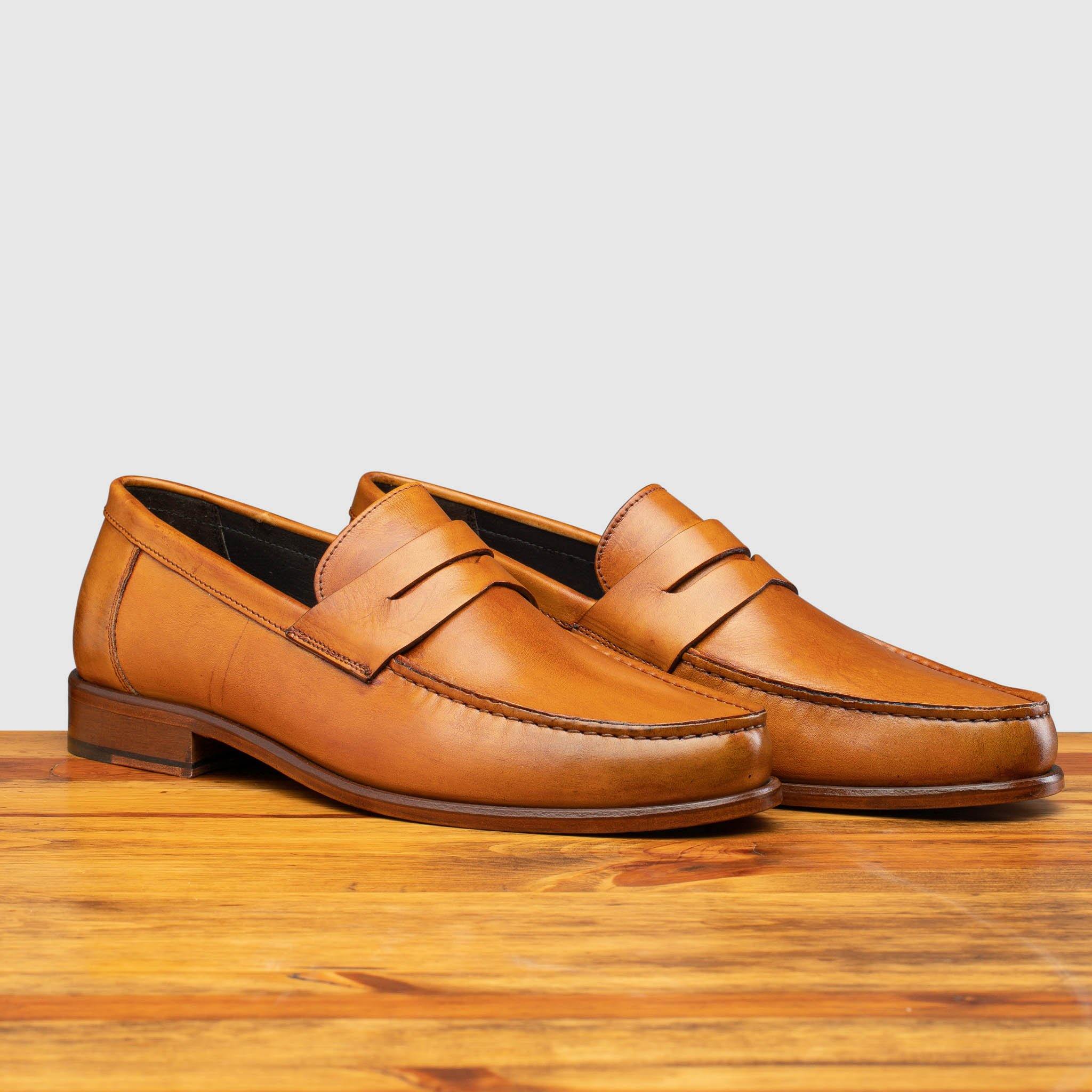 Pair of Dark Caramel leather loafer on a wooden surface with a light gray background