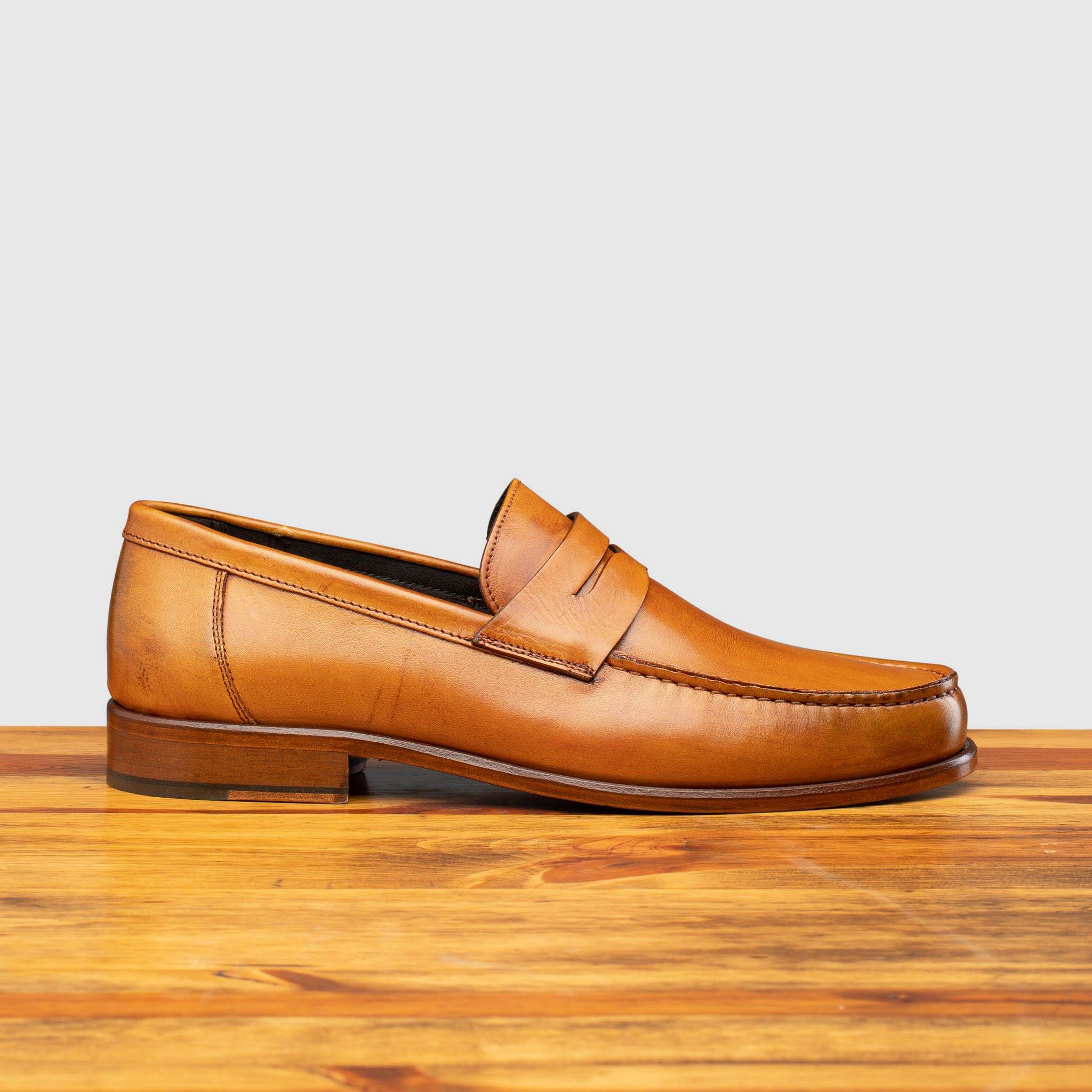 Dark Caramel leather loafer on a wooden surface with a light gray background