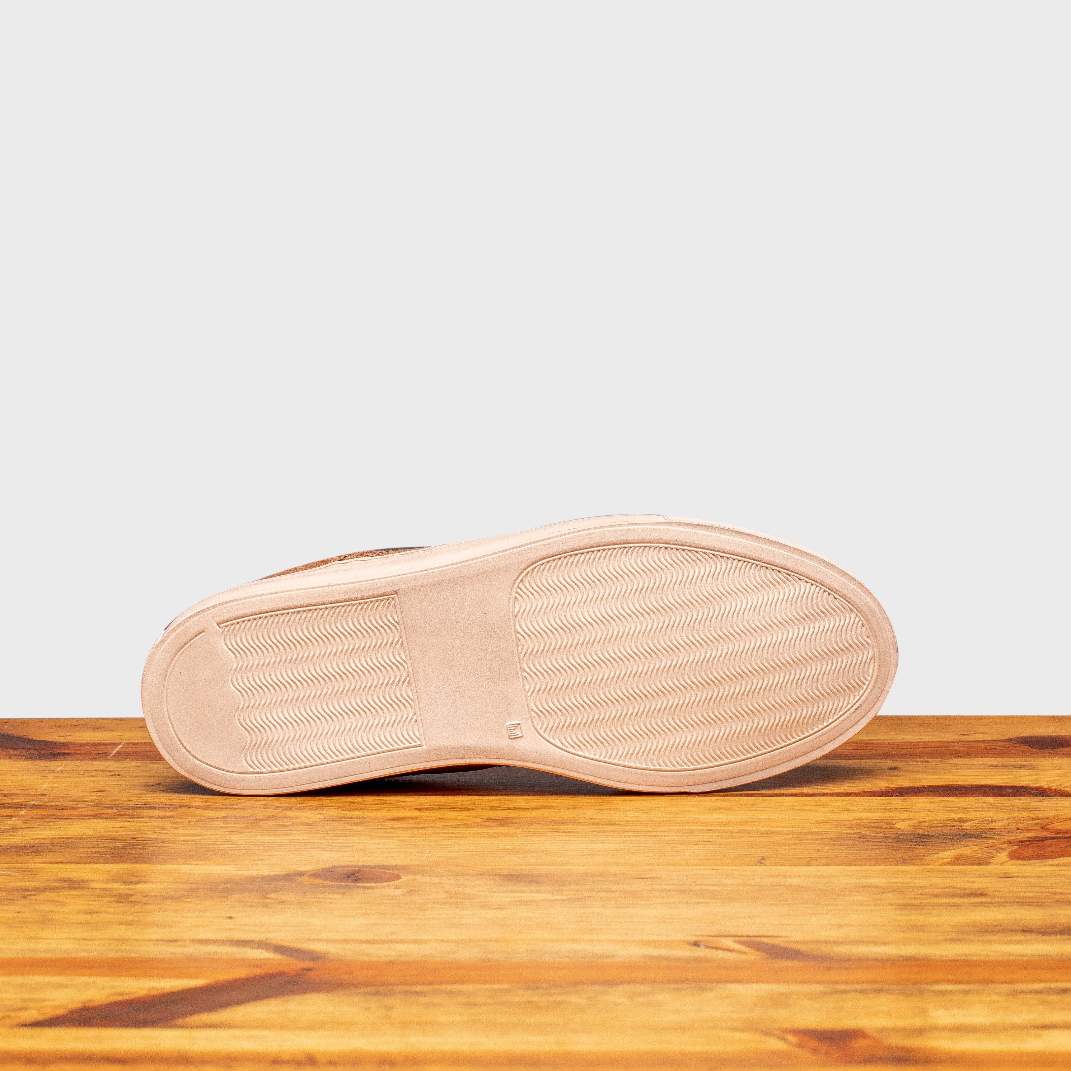Outsole of Brown leather shoe on a wooden surface with a light gray background