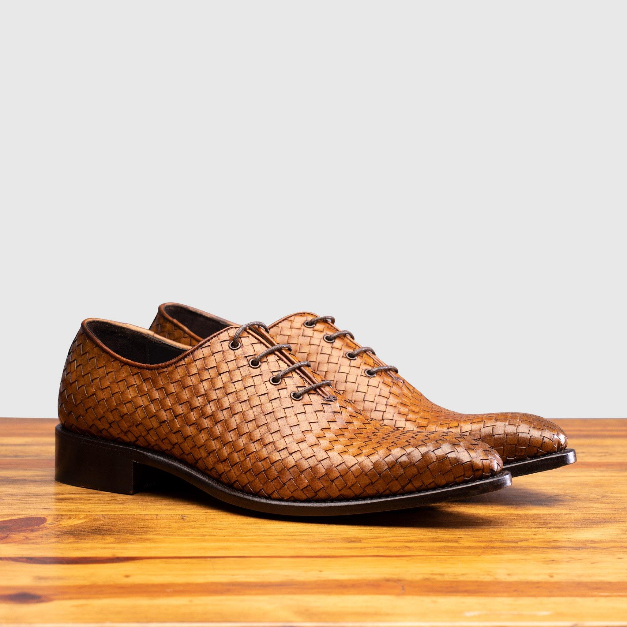 A Pair of Chestnut woven dress shoe on a wooden surface with a light gray background