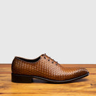 Chestnut woven dress shoe on a wooden surface with a light gray background