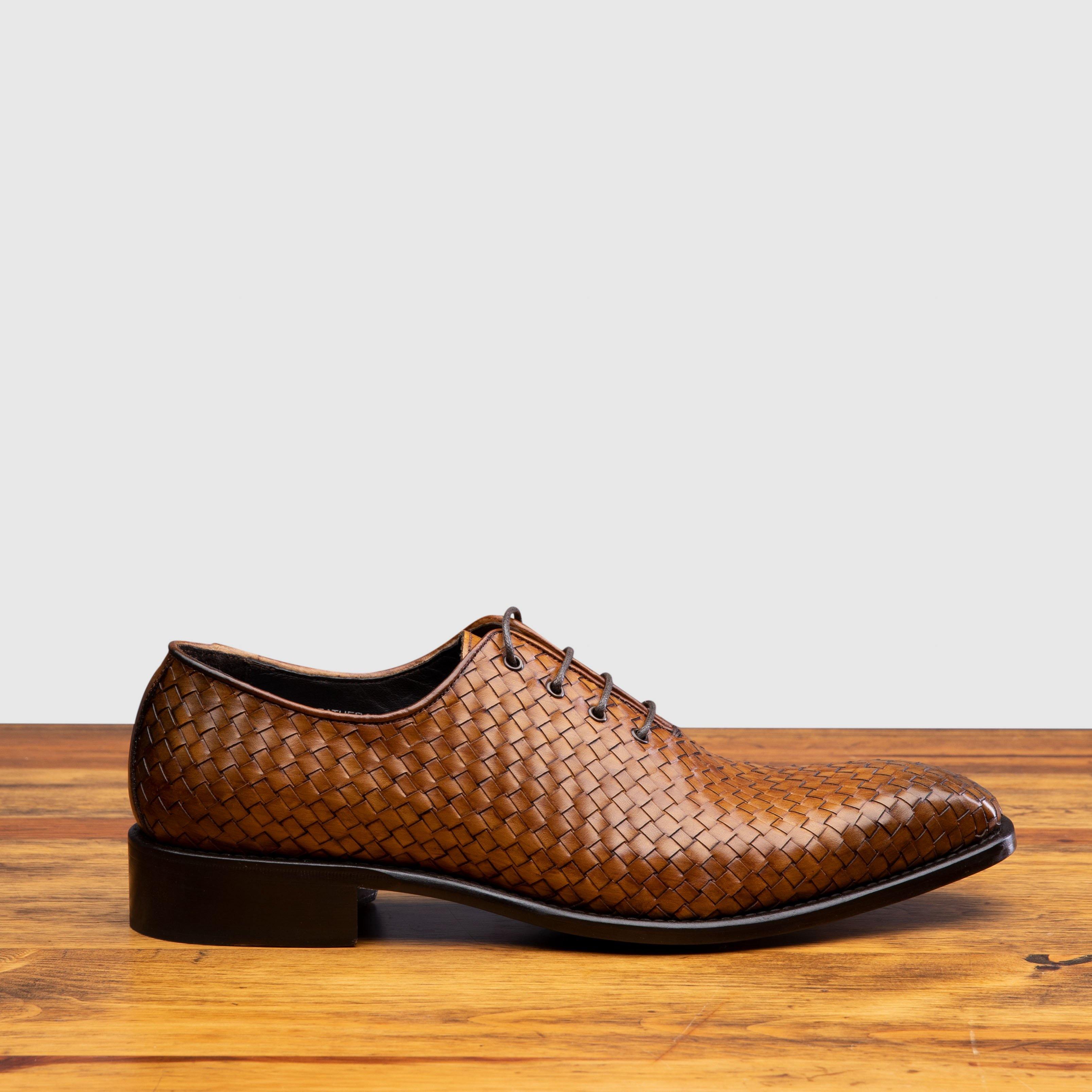 Chestnut woven dress shoe on a wooden surface with a light gray background