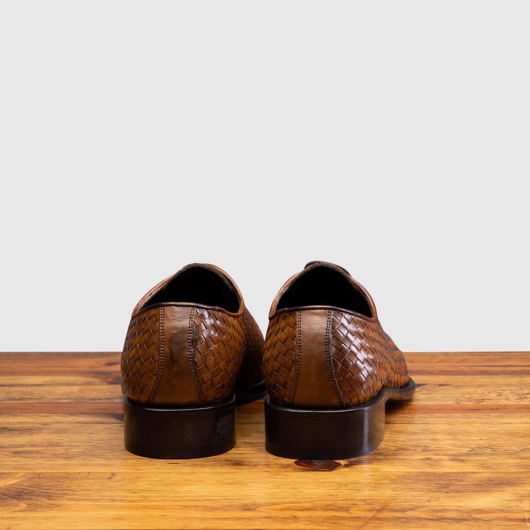 A Pair of Chestnut woven dress shoe on a wooden surface with a light gray background