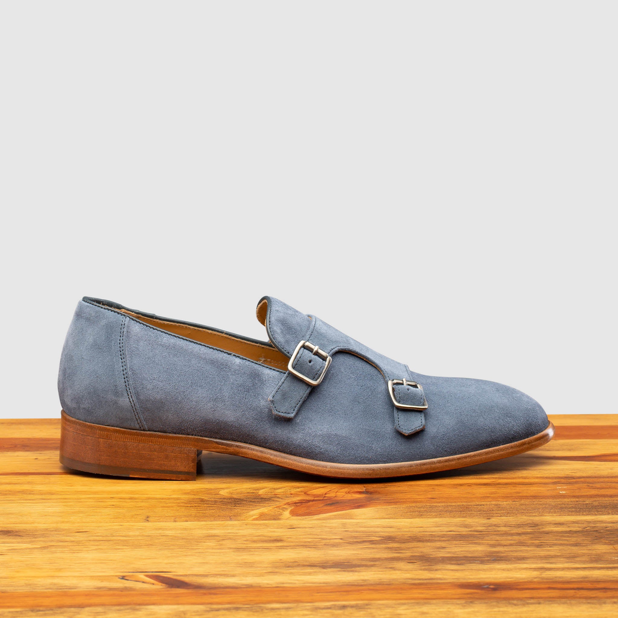 Blue suede loafer with brown sole on a wooden surface