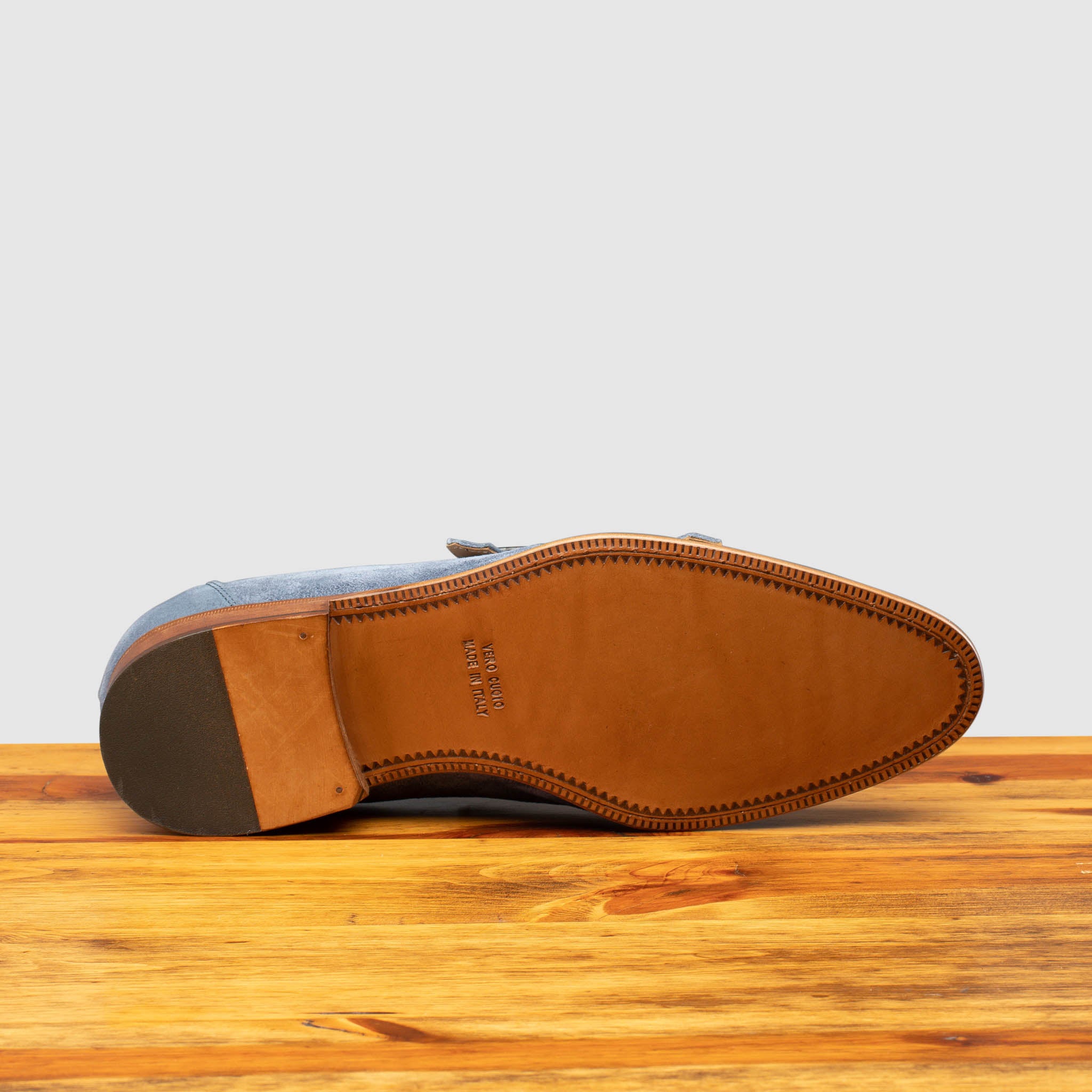 Outsole of Blue suede loafer with brown sole on a wooden surface