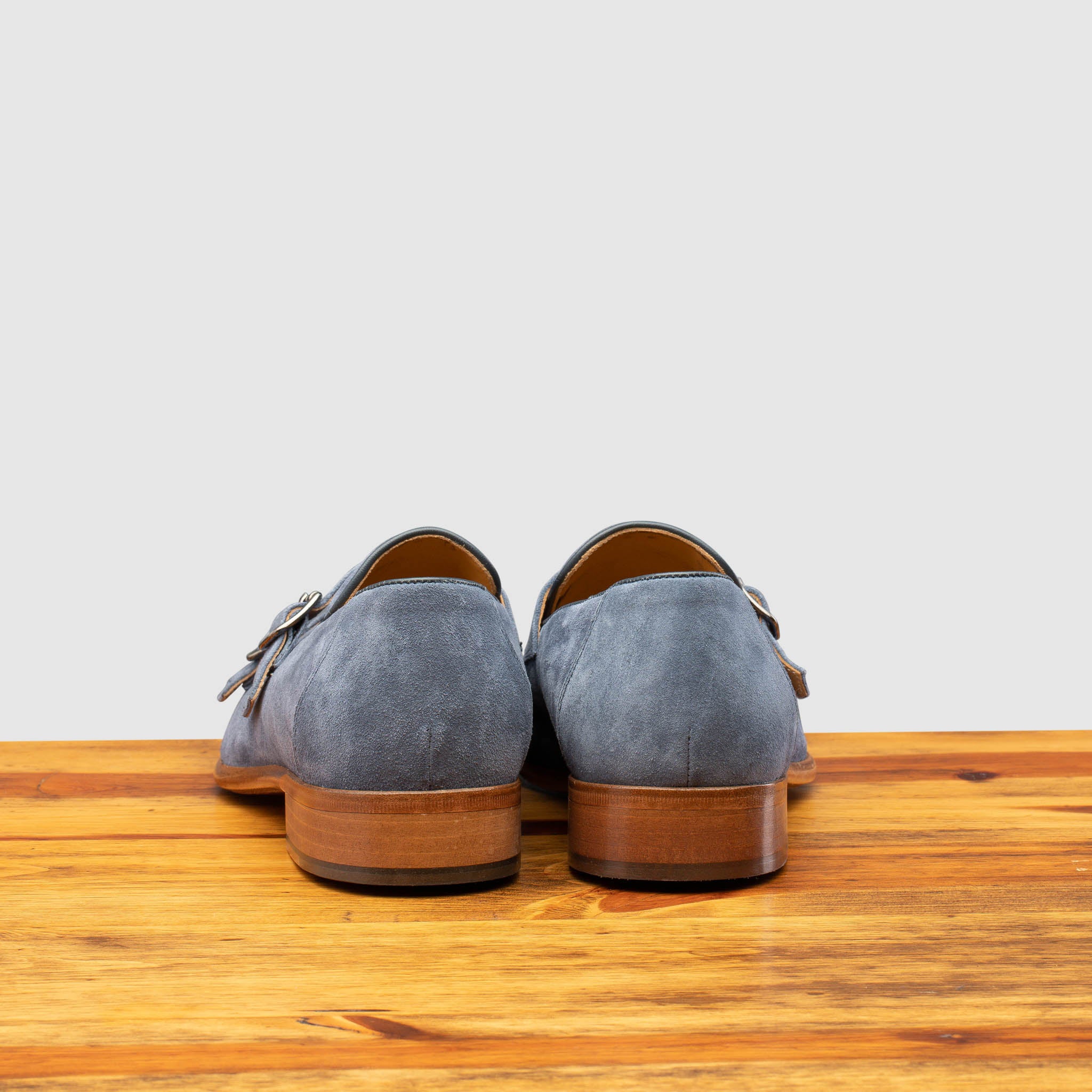 Back view of Blue suede loafer with brown sole on a wooden surface