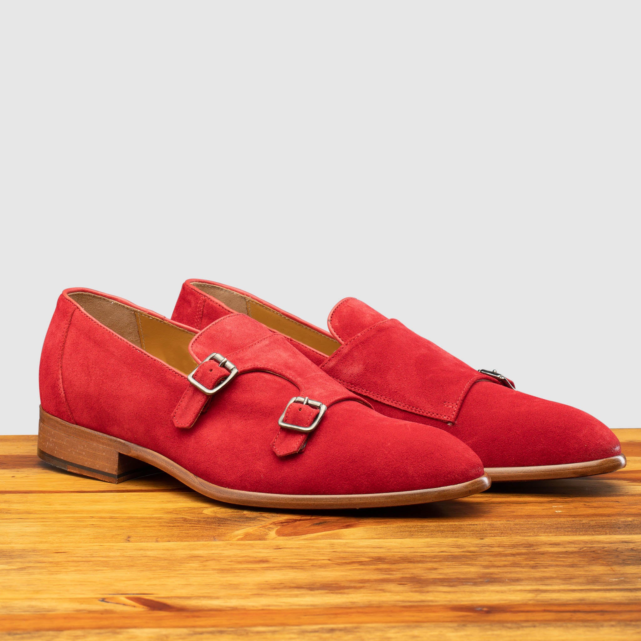 A Pair of Red suede loafer with brown sole on a wooden surface