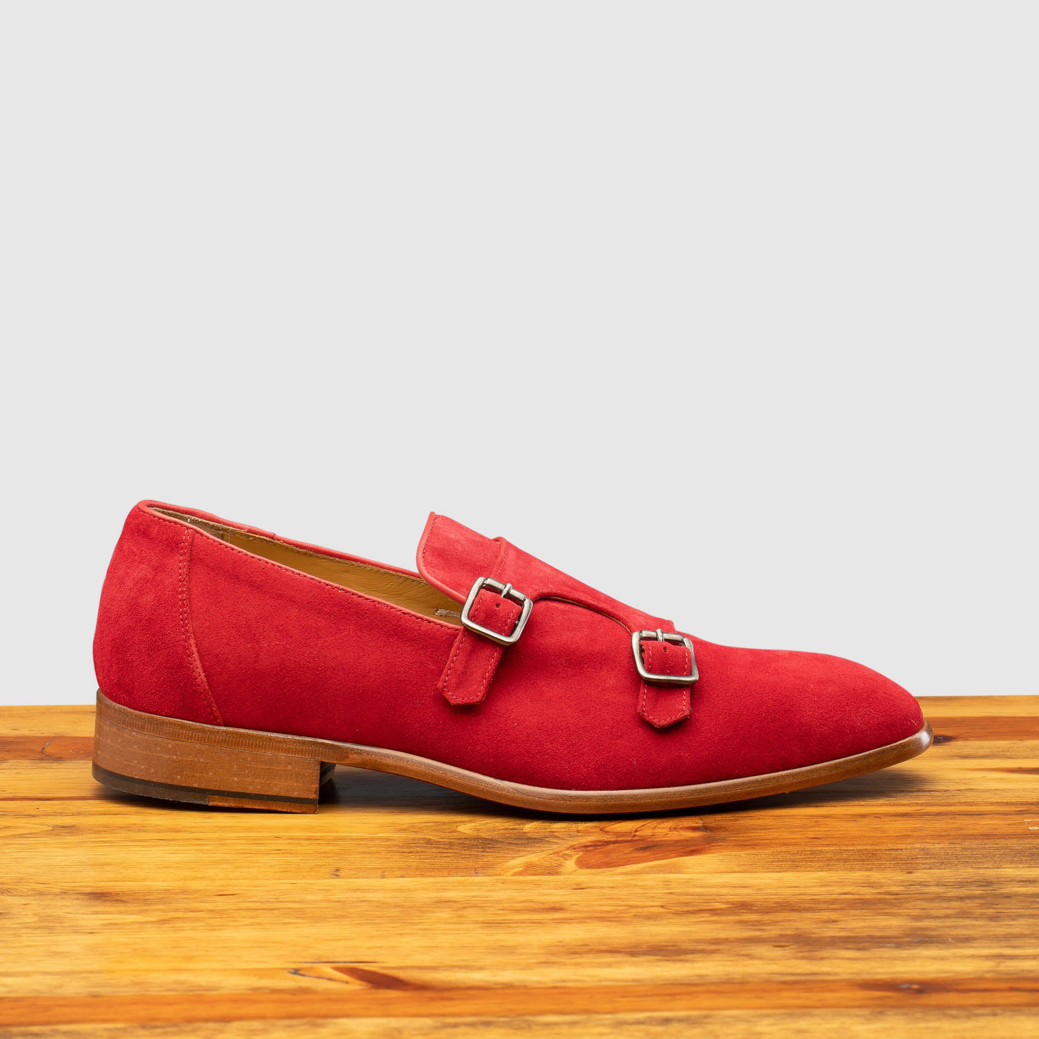 Red suede loafer with brown sole on a wooden surface