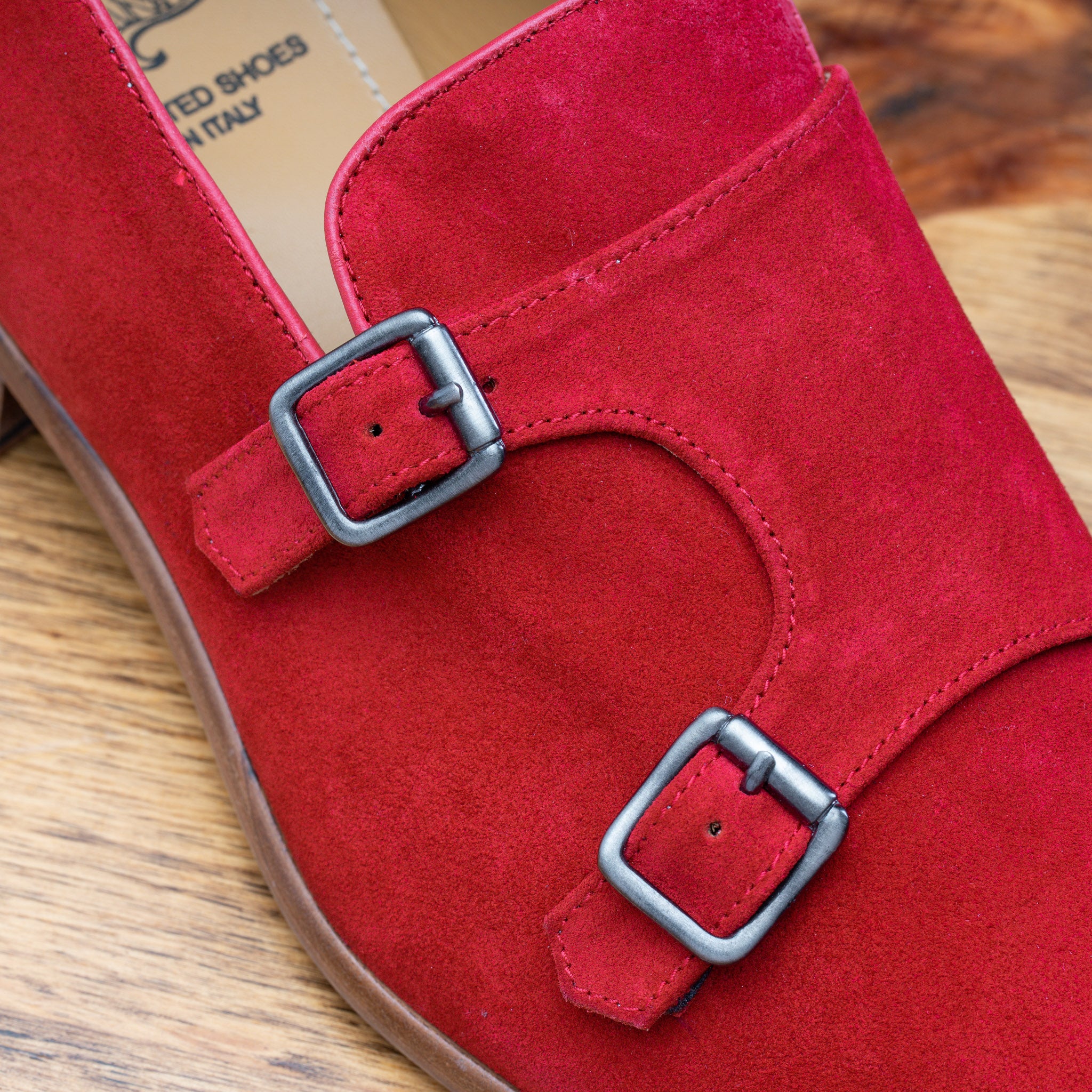 Close view of Red suede loafer with brown sole on a wooden surface