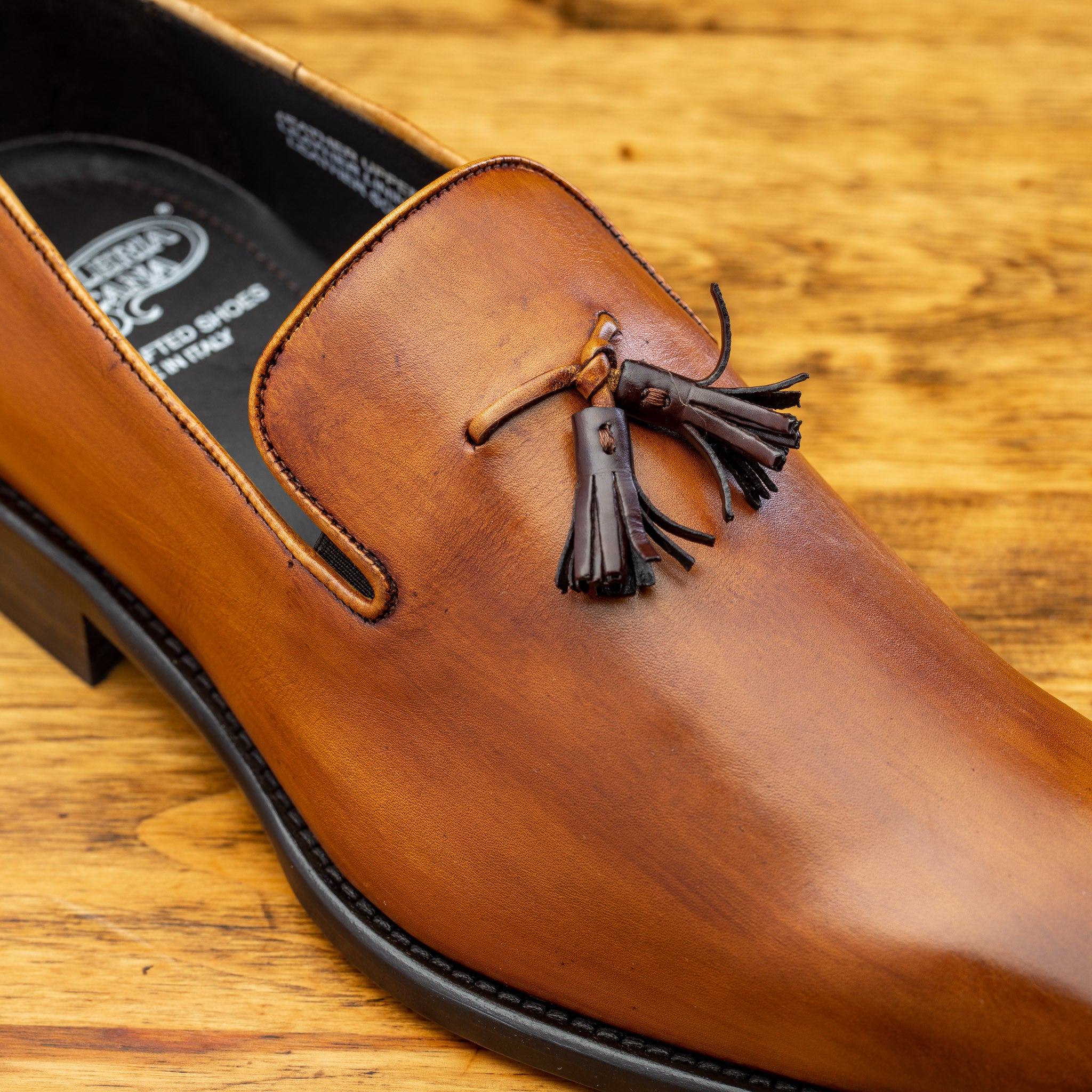 Close view of Caramel leather loafer with a tassel on a wooden surface