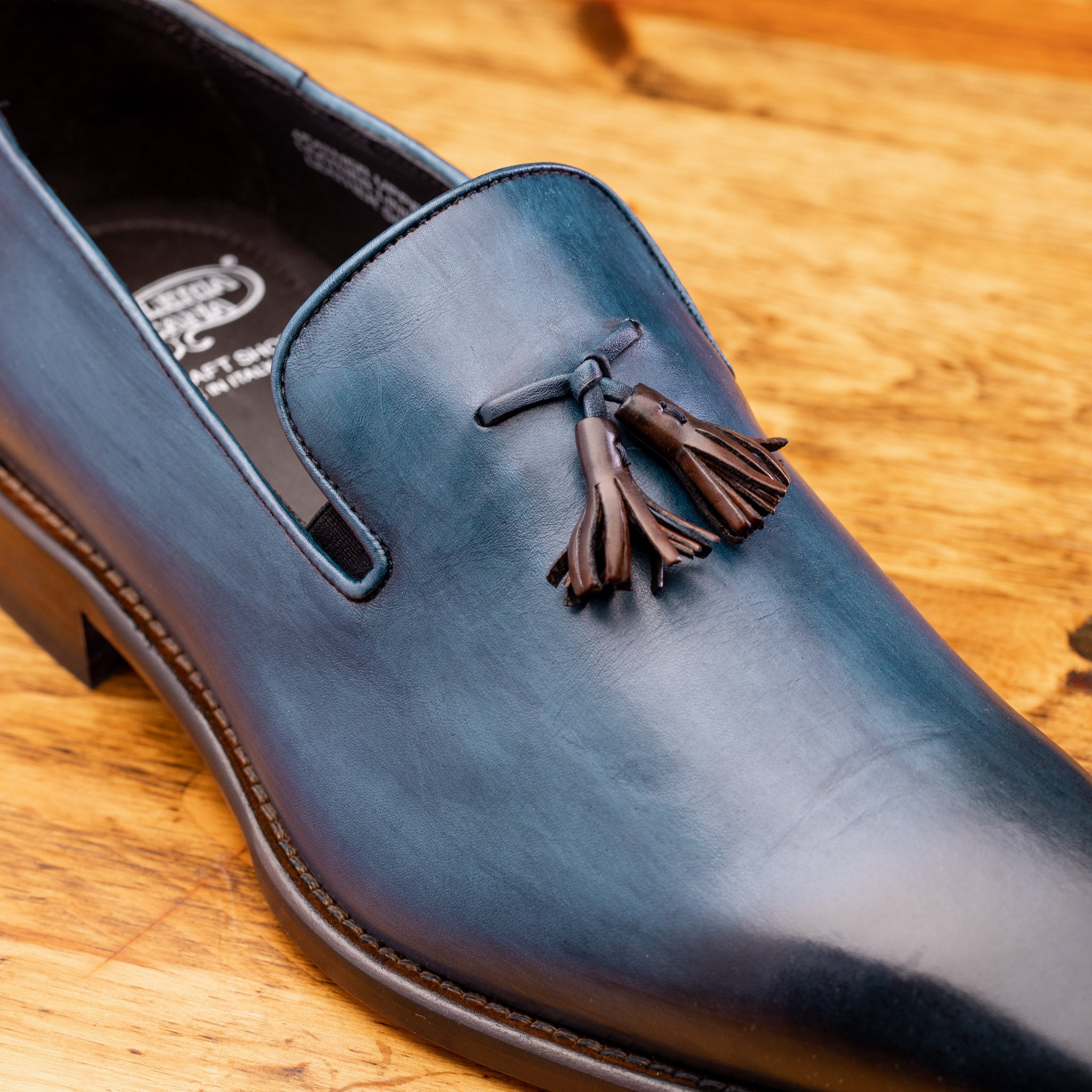 Close view of Blue leather loafer with a tassel on a wooden surface