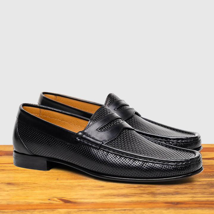 Pair of Black leather loafer on a wooden surface with a light gray background