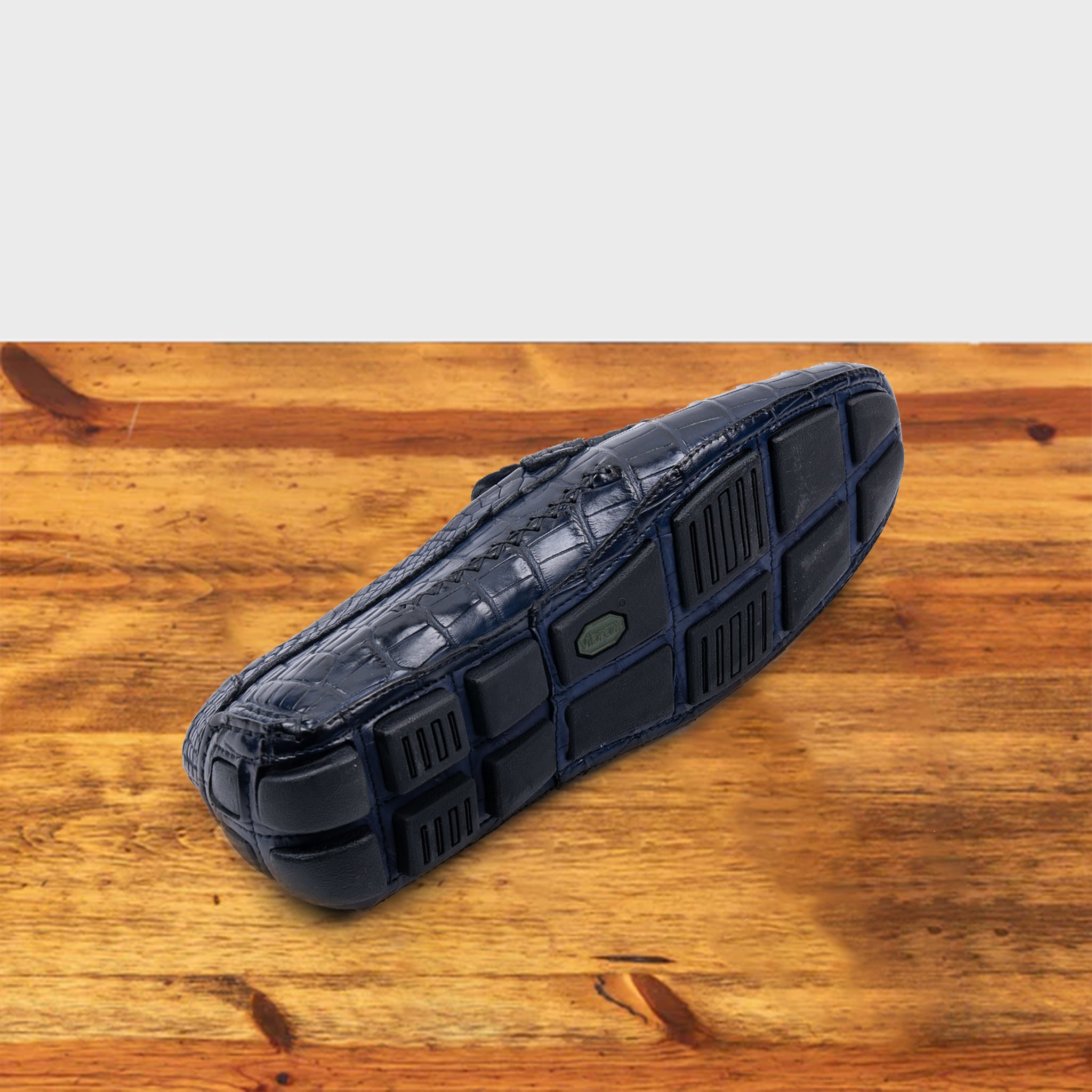 Outsole of Blue crocodile-patterned loafer on a wooden surface with a light gray background