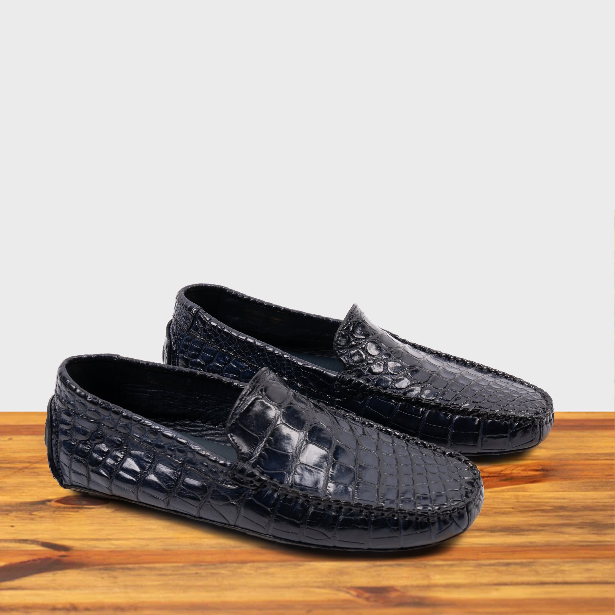 A Pair of Blue crocodile-patterned loafer on a wooden surface with a light gray background