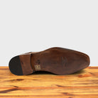 Outsole of Caramel leather dress shoe on a wooden surface with a light gray background