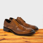 Caramel leather dress shoe on a wooden surface with a light gray background