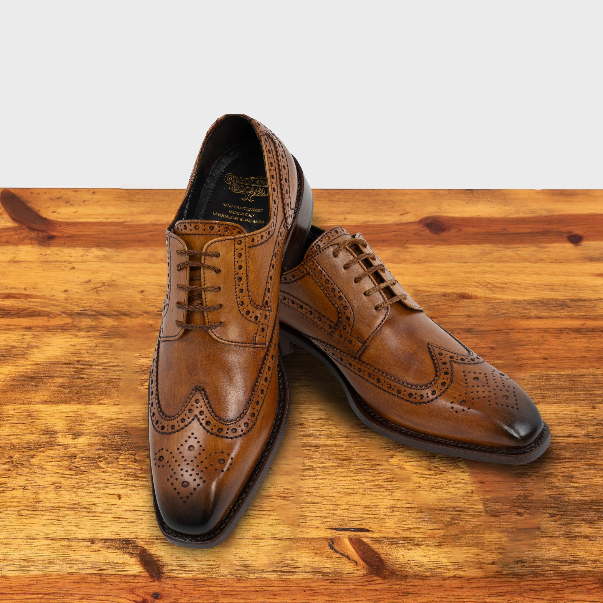Caramel leather dress shoe on a wooden surface with a light gray background